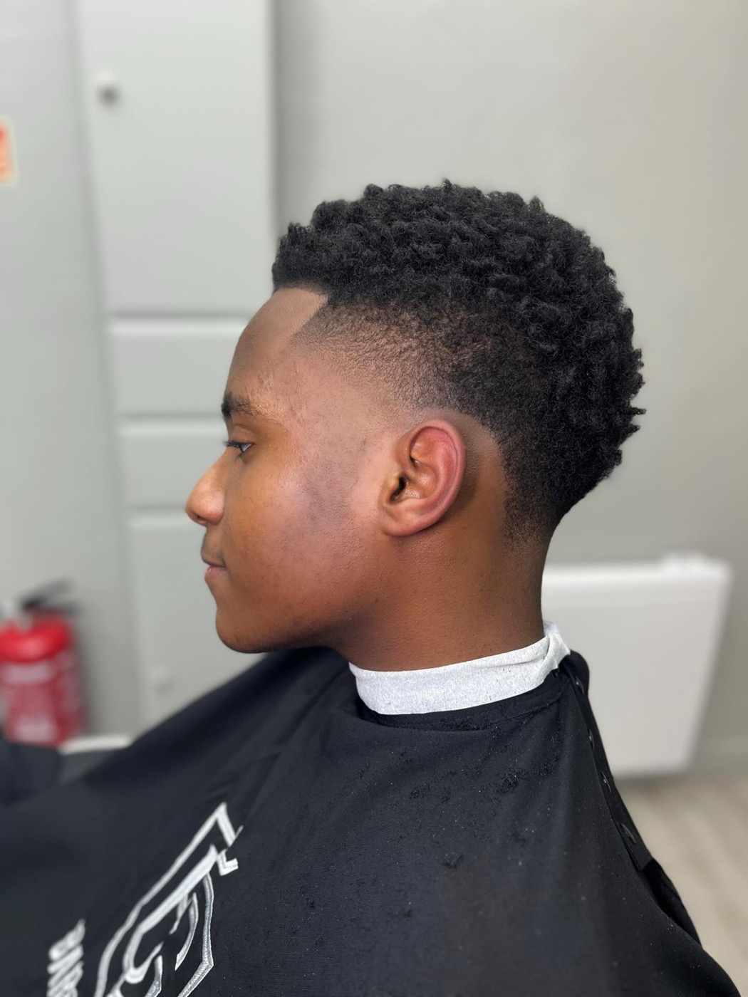 Coupe sur cheveux crépus avec volume sur le dessus, dégradé fondu et contour tracé à la lame, réalisée chez BG Barbershop à Beynes