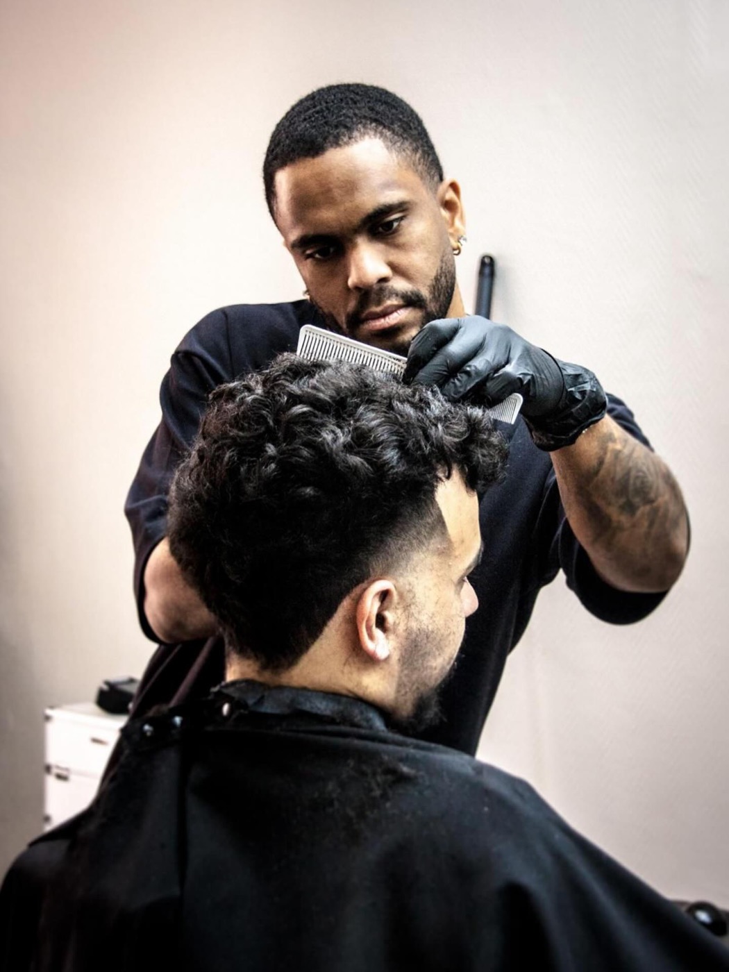 Barbier de BG Barbershop à Beynes travaillant le dessus d'un client au peigne, cuir chevelu net et cape noire sans pellicules